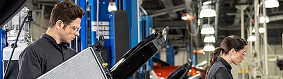 Two technicians, a man and a woman, working on cars in a car service workshop